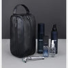 A black leather travel cosmetic bag is shown with a bottle of Blue Man skin product and a silver grooming tool.