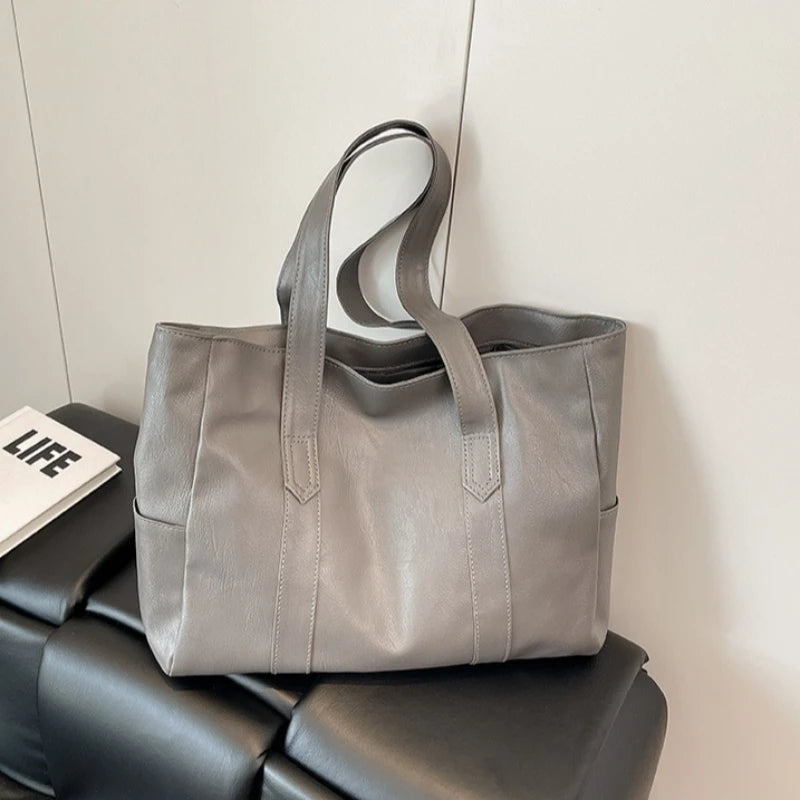 A gray vintage-style zip-top tote bag made of durable vegan leather resting on a black surface.