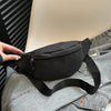 Une main tient un sac bandoulière noir en nylon contre une chemise en jean gris.