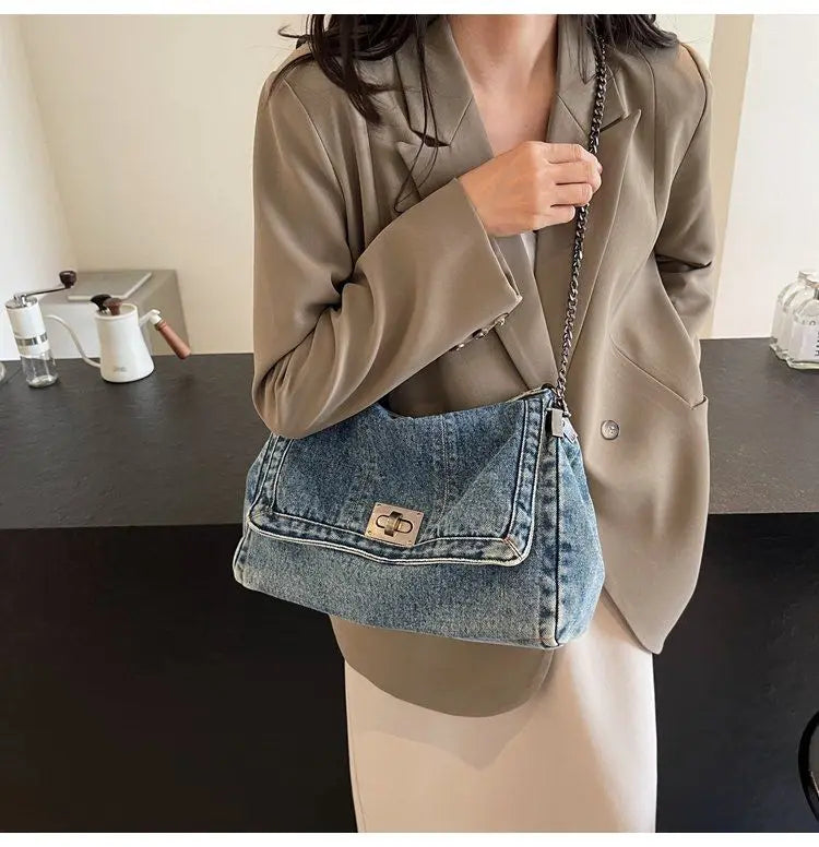 A woman wearing a beige blazer and light pants holds a denim tote bag with a silver chain strap.