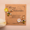 A handmade card featuring a yellow flower and bee-shaped keychains with the text Always Remember