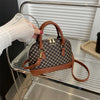 A brown leather fashion shell shoulder crossbody bag with gold hardware resting on a silver metal tray.