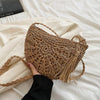 A close-up of a handmade rattan straw crossbody bag being held against a white sheet.