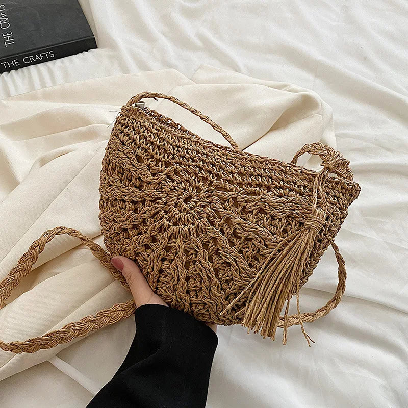 A close-up of a handmade rattan straw crossbody bag being held against a white sheet.
