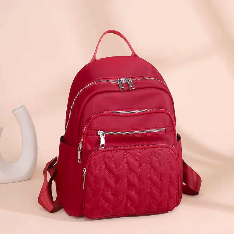 A red quilted waterproof women's travel backpack with zippers is shown against a light background.