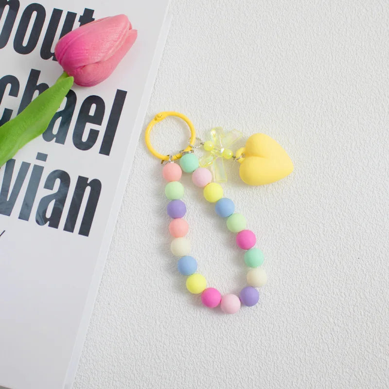 A colorful bead necklace featuring pink, yellow, and green beads with a heart charm on a gold-colored O-ring clip.