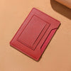 Portefeuille de voyage fin en cuir rose plié et posé sur une surface beige.