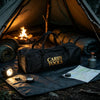 A black storage tote labeled Carry Tools is laid on a ground mat inside a tent next to a campfire.
