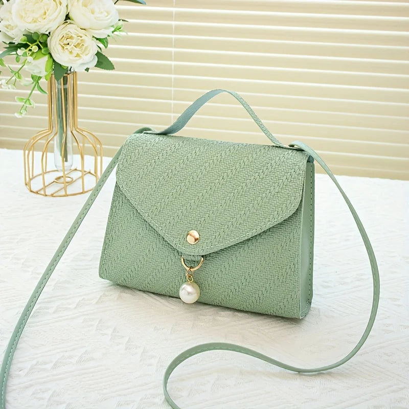 A mint green beaded square crossbody bag with a gold chain and adjustable strap resting on a white surface.