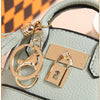 A gold-toned keychain charm featuring a padlock attached to a leather earbud case.