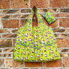 A bright lime green reusable shopping bag featuring a pattern of cute cartoon cats and various colorful icons, displayed agai