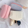 Three quilted cosmetic storage pouches in pink, gray, and cream colors with a silver zipper and a blue accessory.