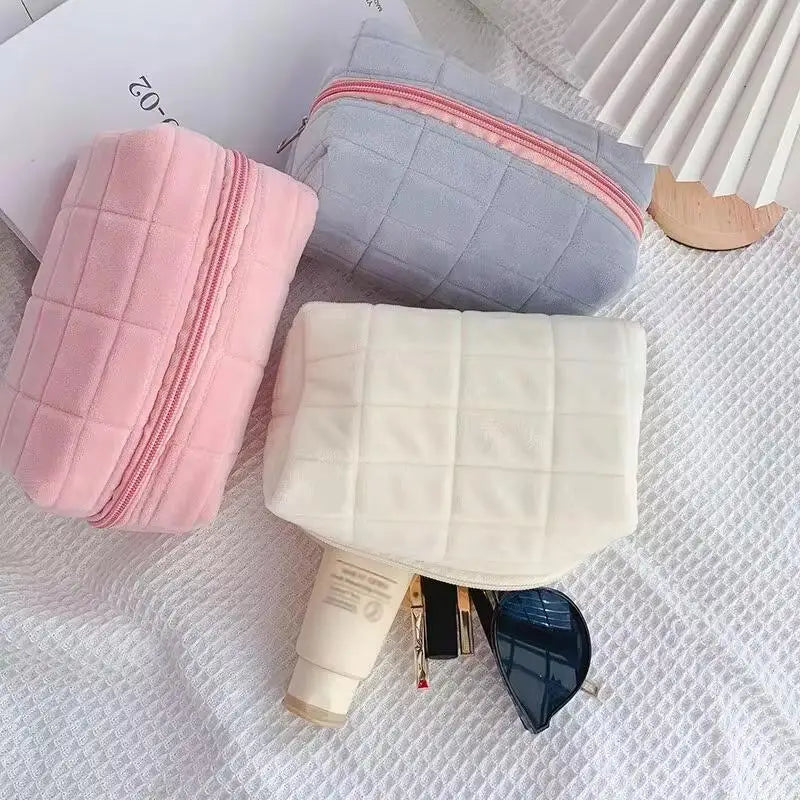 Three quilted cosmetic storage pouches in pink, gray, and cream colors with a silver zipper and a blue accessory.