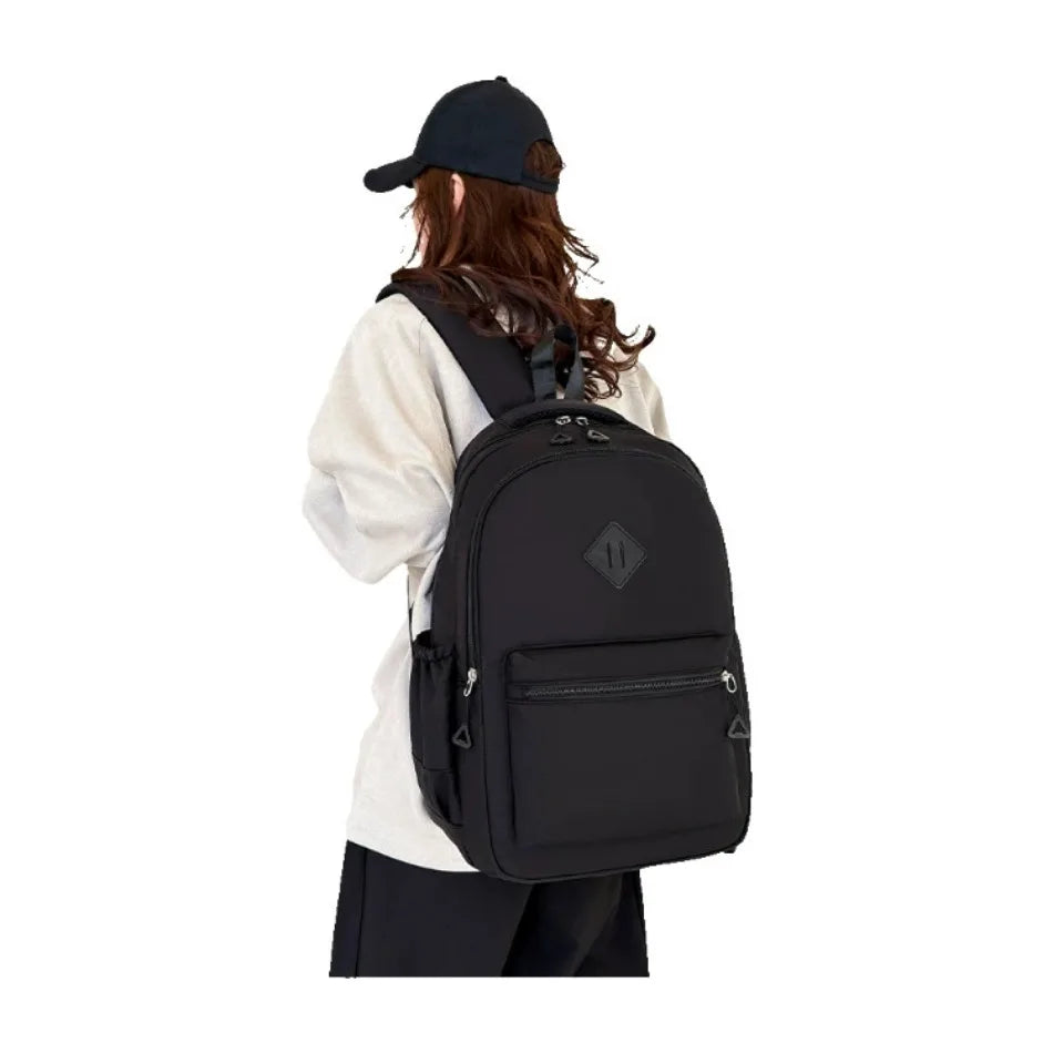 A person wearing a black baseball cap is shown carrying a black durable nylon commuter backpack.
