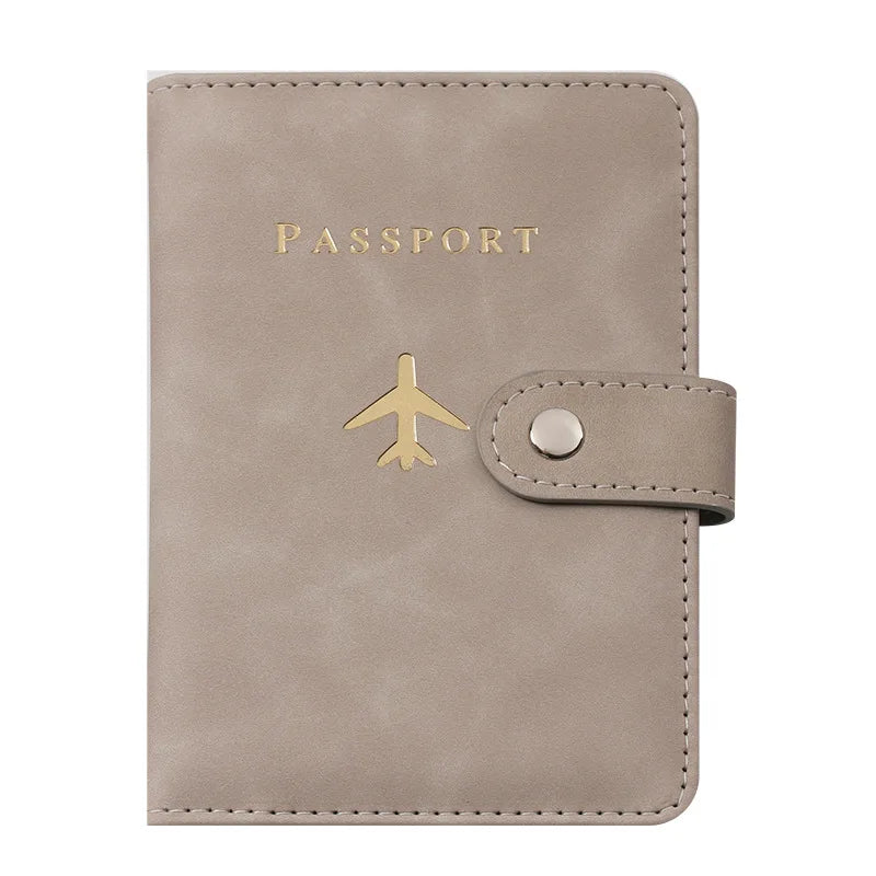 Porte-passeport en cuir beige avec lettres dorées et détail de sangle en cuir.