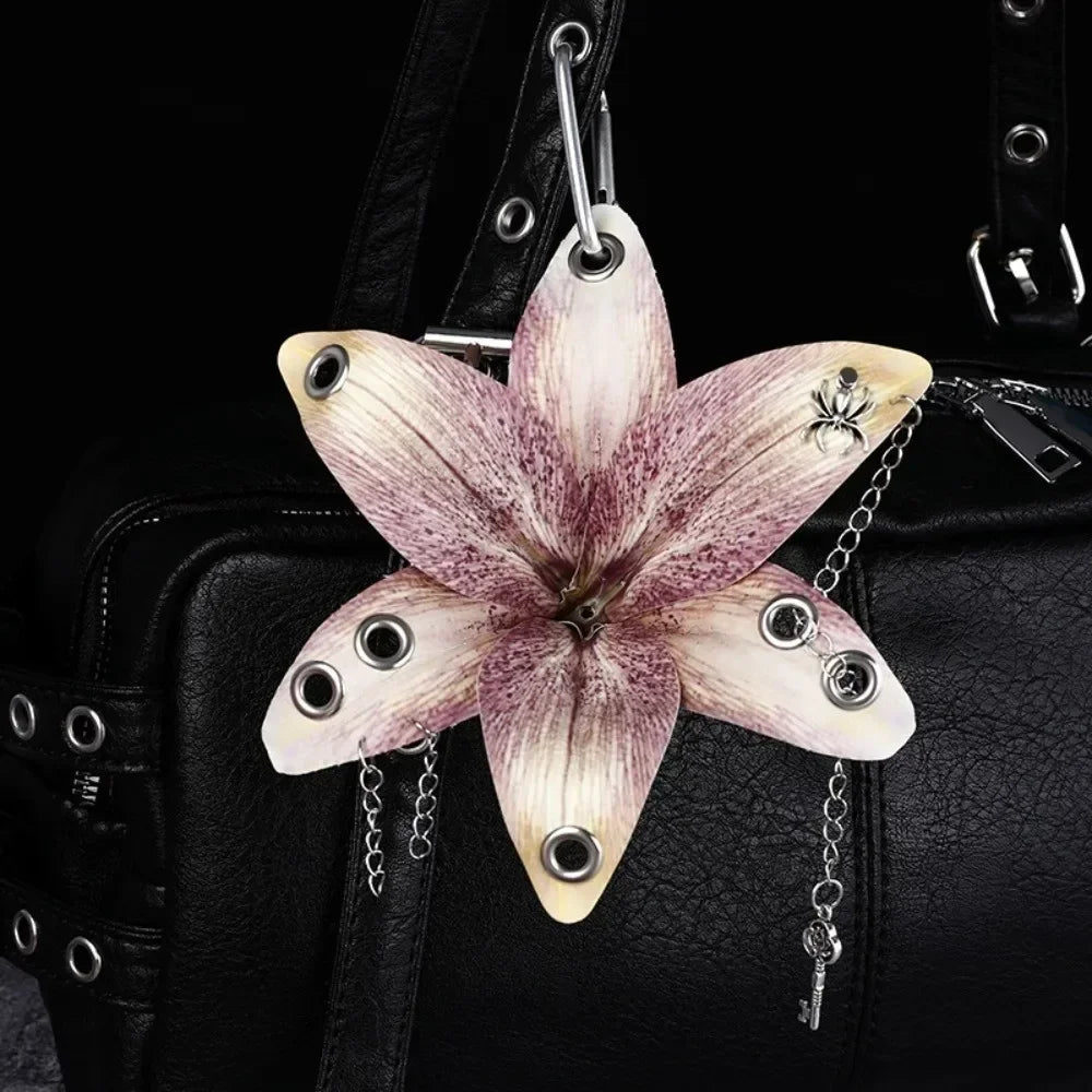 A realistic orchid flower shaped keychain with delicate purple and white petals attached to a black leather bag.