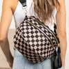 Eine Frau in weißem Oberteil und Jeans hält eine schwarze karierte Crossbodytasche mit Lederriemen.