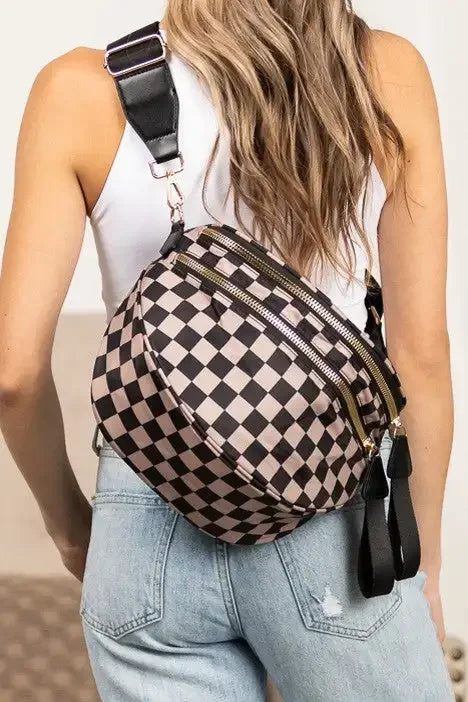 Eine Frau in weißem Oberteil und Jeans hält eine schwarze karierte Crossbodytasche mit Lederriemen.