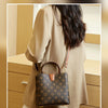 A beige coat features a brown leather bucket bag with a gold-toned strap and a patterned design.