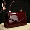 A glossy, deep burgundy evening handbag with a leather texture is displayed on a light wooden surface.