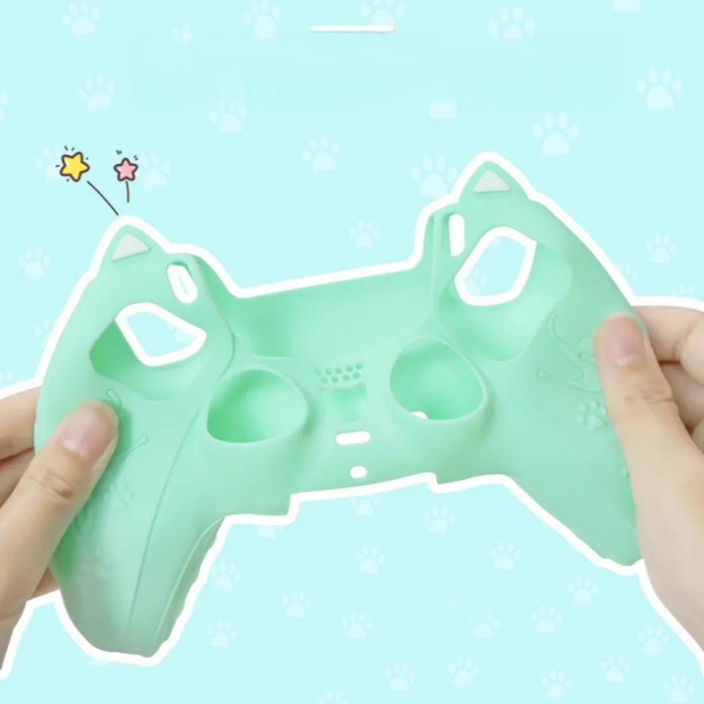 A hand holds a light green silicone grip cover designed for a PS5 controller, featuring paw print decorations.