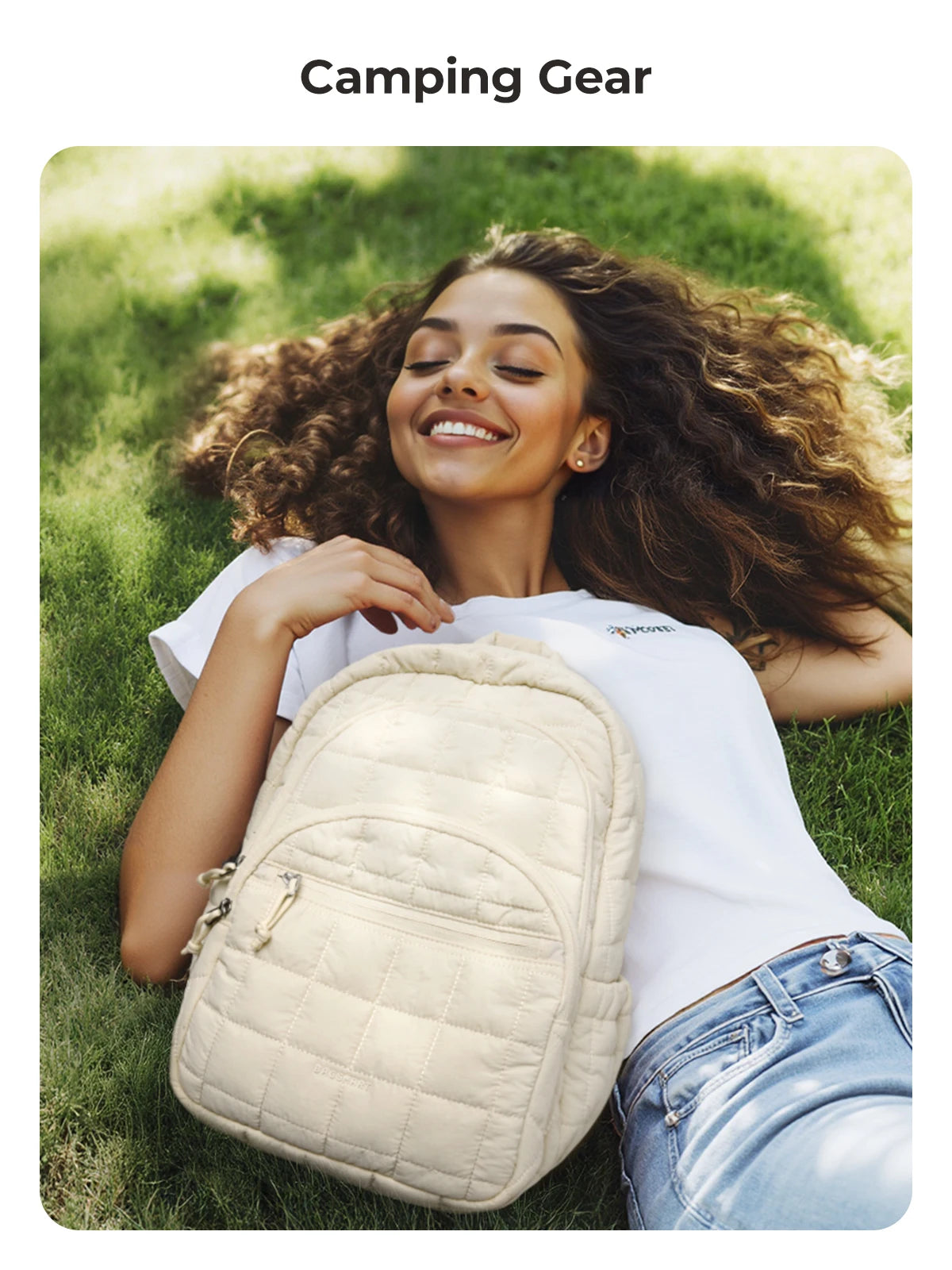 A woman is smiling while holding a beige quilted casual backpack outdoors on green grass.