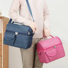 A person is holding a navy blue reusable insulated lunch bag and a pink reusable insulated lunch bag.