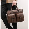 A brown men's PU leather business briefcase bag being held by a person wearing black pants and a beige jacket.