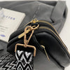 Black vegan PU crossbody bag with gold hardware and a black and white patterned strap.