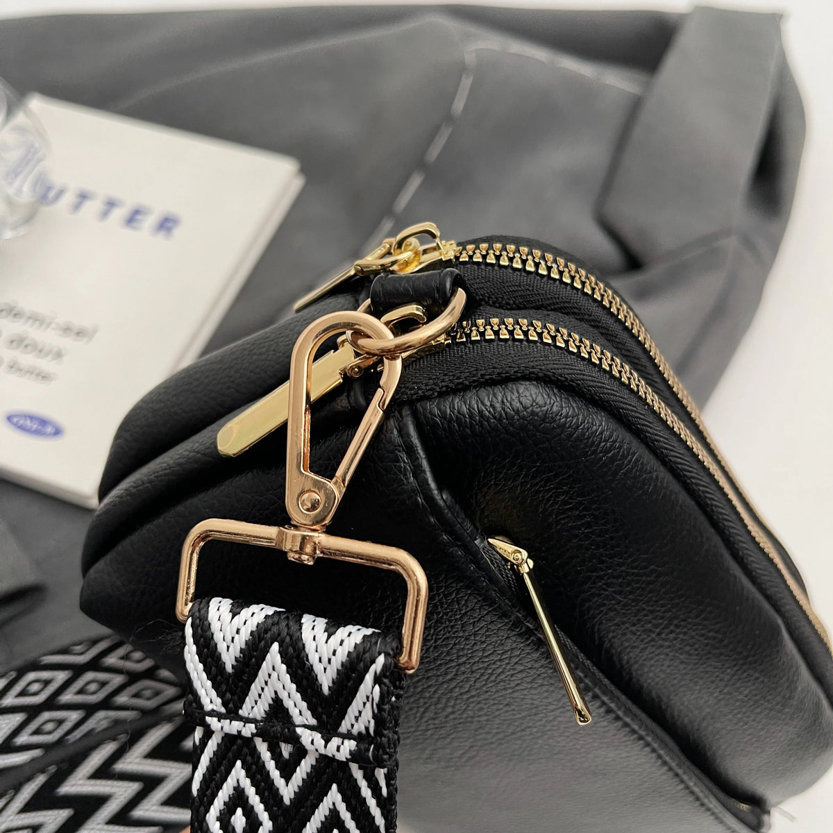 Black vegan PU crossbody bag with gold hardware and a black and white patterned strap.