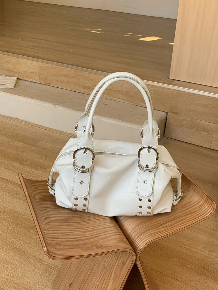 A white PU leather shoulder bag with silver rivets resting on a light wooden surface.