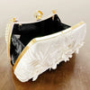A white clutch bag with gold trim and pearl detailing, featuring embroidered floral texture.