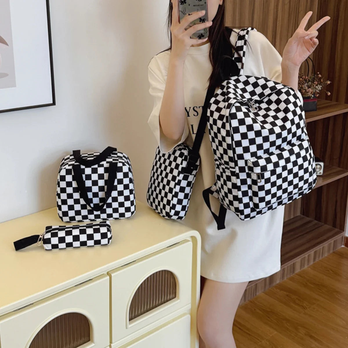 A person is holding a black and white checkerboard multi-pocket backpack in a light-colored outfit.