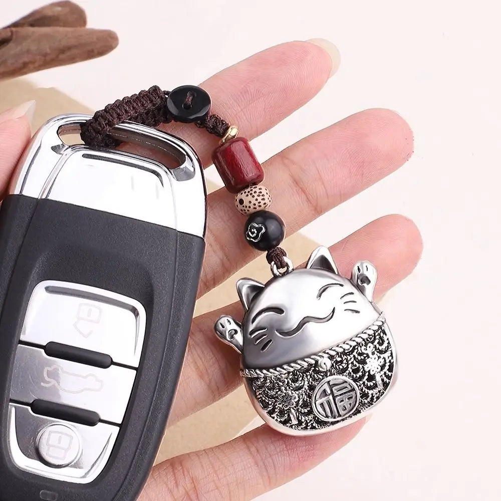 A hand holds a silver and black key ring keychain featuring a detailed cat design and beaded chain.