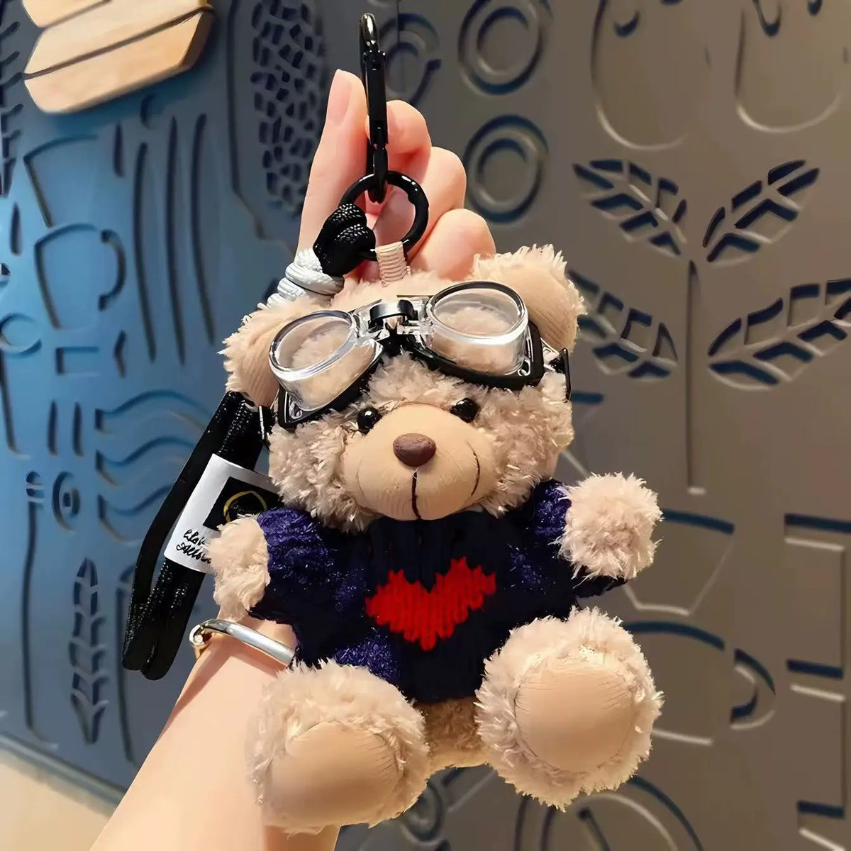 A charming plush bear keychain featuring a camera and glasses attached to a black strap.