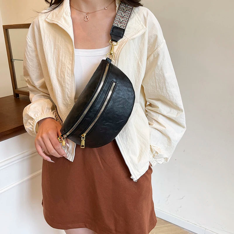 A woman wearing a beige jacket and brown skirt holds a black PU leather crossbody bag with a gold chain strap.