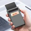 A hand holds a slim metal pop-up card holder wallet with a ten dollar bill inside.