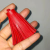 A hand holds a bright red leather tassel fringe craft supply set.