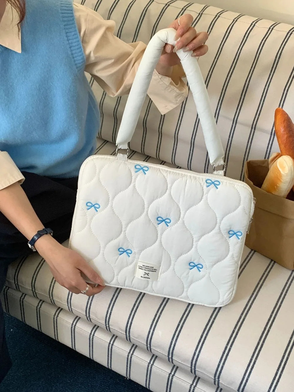 Bolso para portátil acolchado blanco con detalles de lazo azul claro sobre una superficie a rayas.