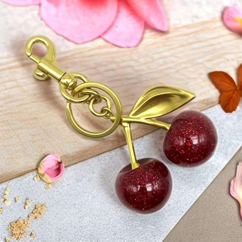 Gold-toned crystal fruit charm keychain featuring a shiny red apple on a light background.