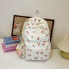 A white corduroy fashion backpack with a red cherry pattern is displayed on a white surface.