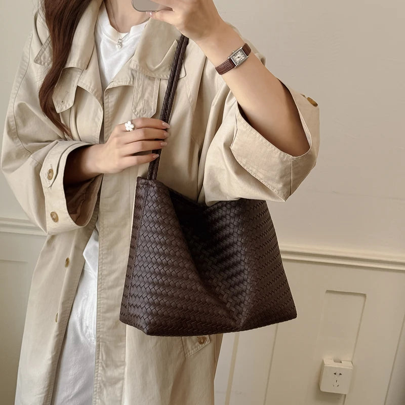 A woman wearing a beige trench coat holds a dark brown PU bucket shoulder bag.