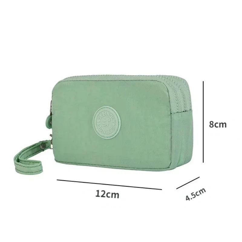A light green compact three-layer nylon zipper pouch with a circular logo and a strap.