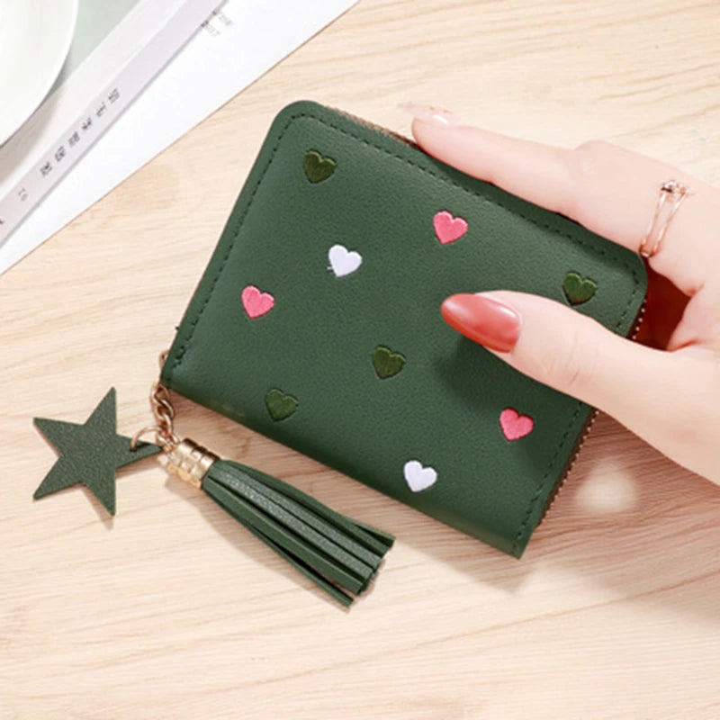 A dark green compact PU leather wallet with a zipper closure decorated with small pink and white heart shapes and a gold tass