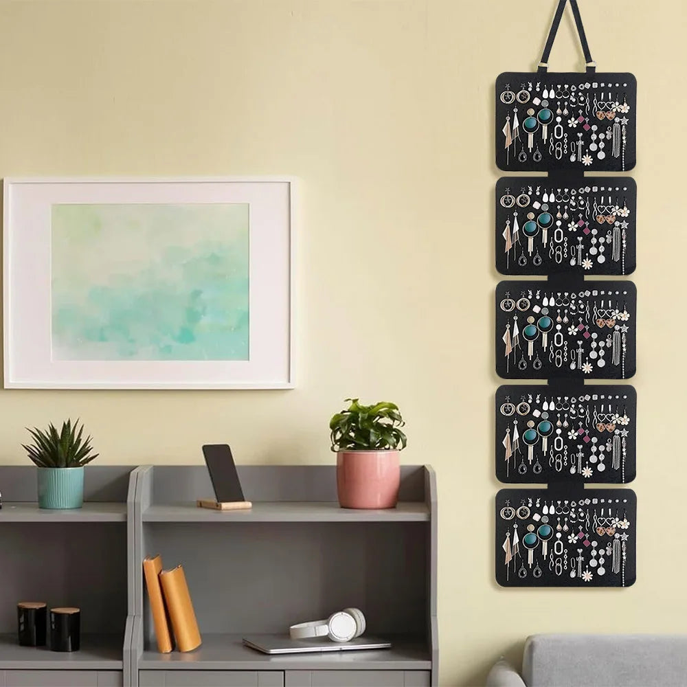 A black wall-mounted organizer with five layers of hooks and jewelry displayed on a light yellow wall.