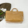 Un bolso tote minimalista de PVC marrón junto a una chaqueta verde oliva doblada y tulipanes blancos.