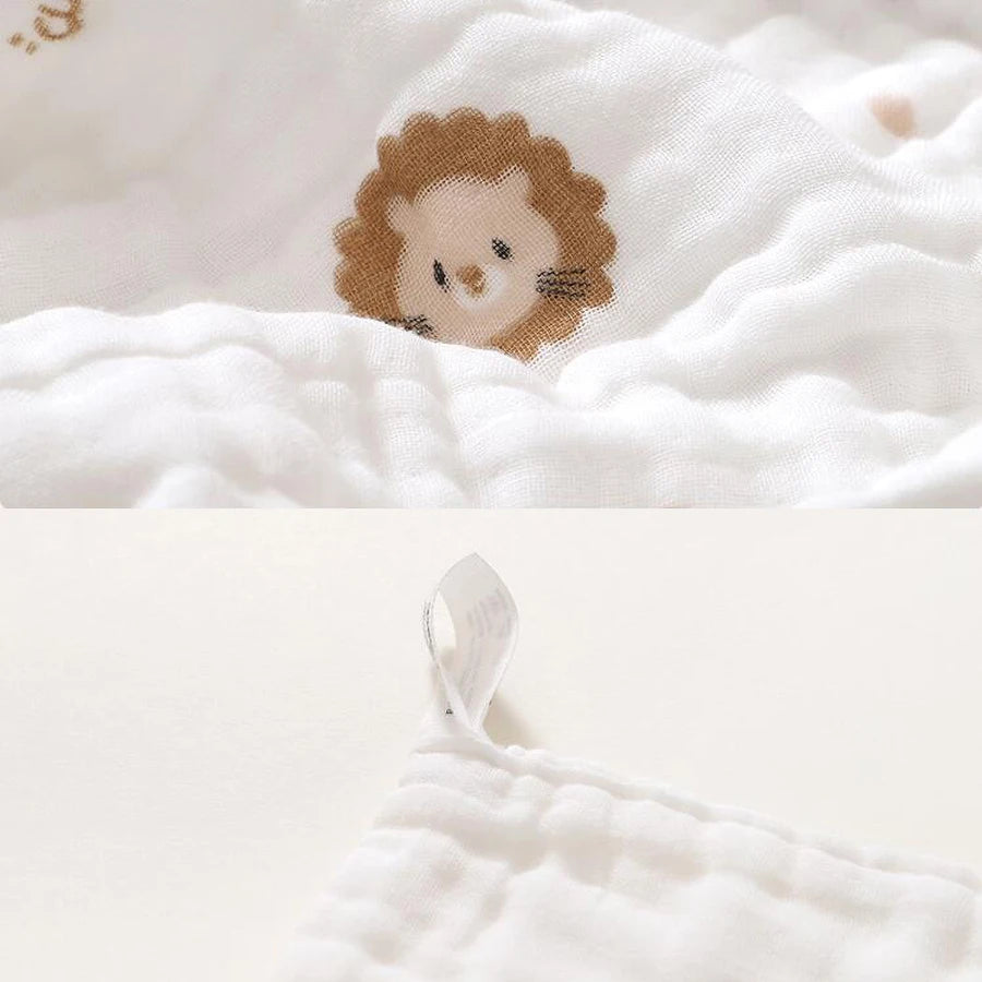 A close-up of a white muslin baby burp cloth towel featuring a cute lion face print.