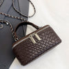 A dark brown crocodile-textured woven crossbody bag with a silver zipper and chain strap resting on a gray envelope.