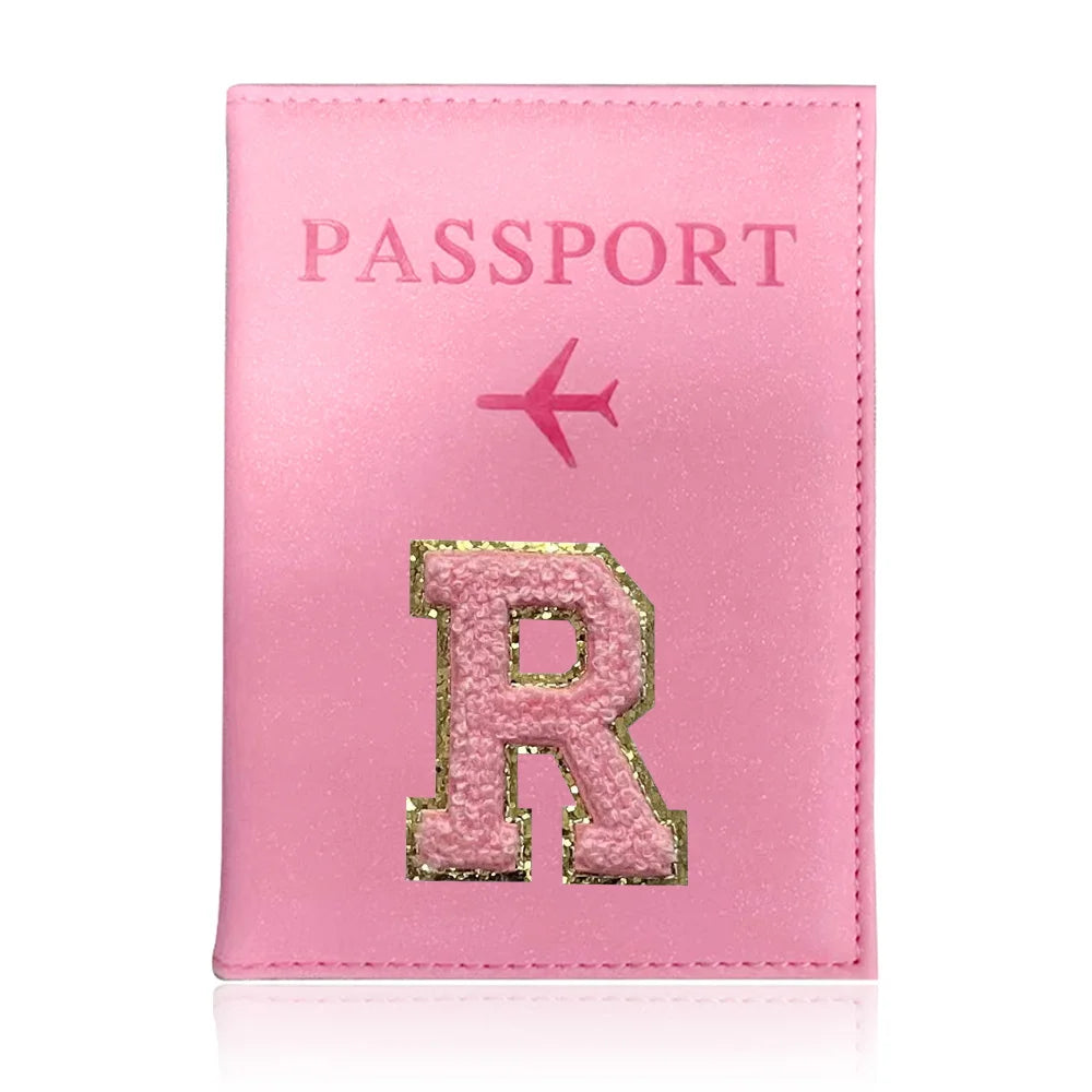 A pink leather passport holder with a gold initial R and a pink airplane symbol.