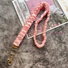 Pinkes Rüschen-Lanyard mit goldenem Schlüsselclip auf grauer strukturierter Oberfläche.